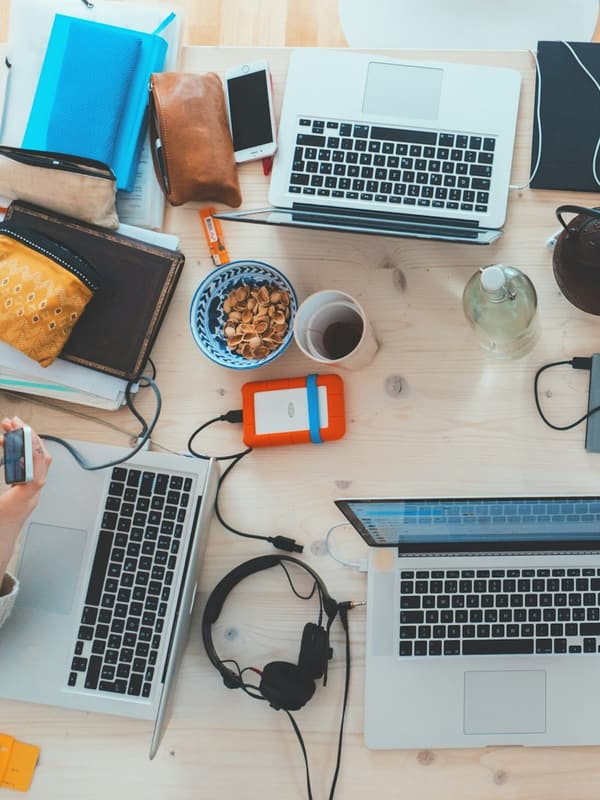 Laptops, notebooks and a phone on a shared wooden desk, seen from above